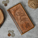 Brown leather bifold wallet with a tooled floral design, lying closed on a table.