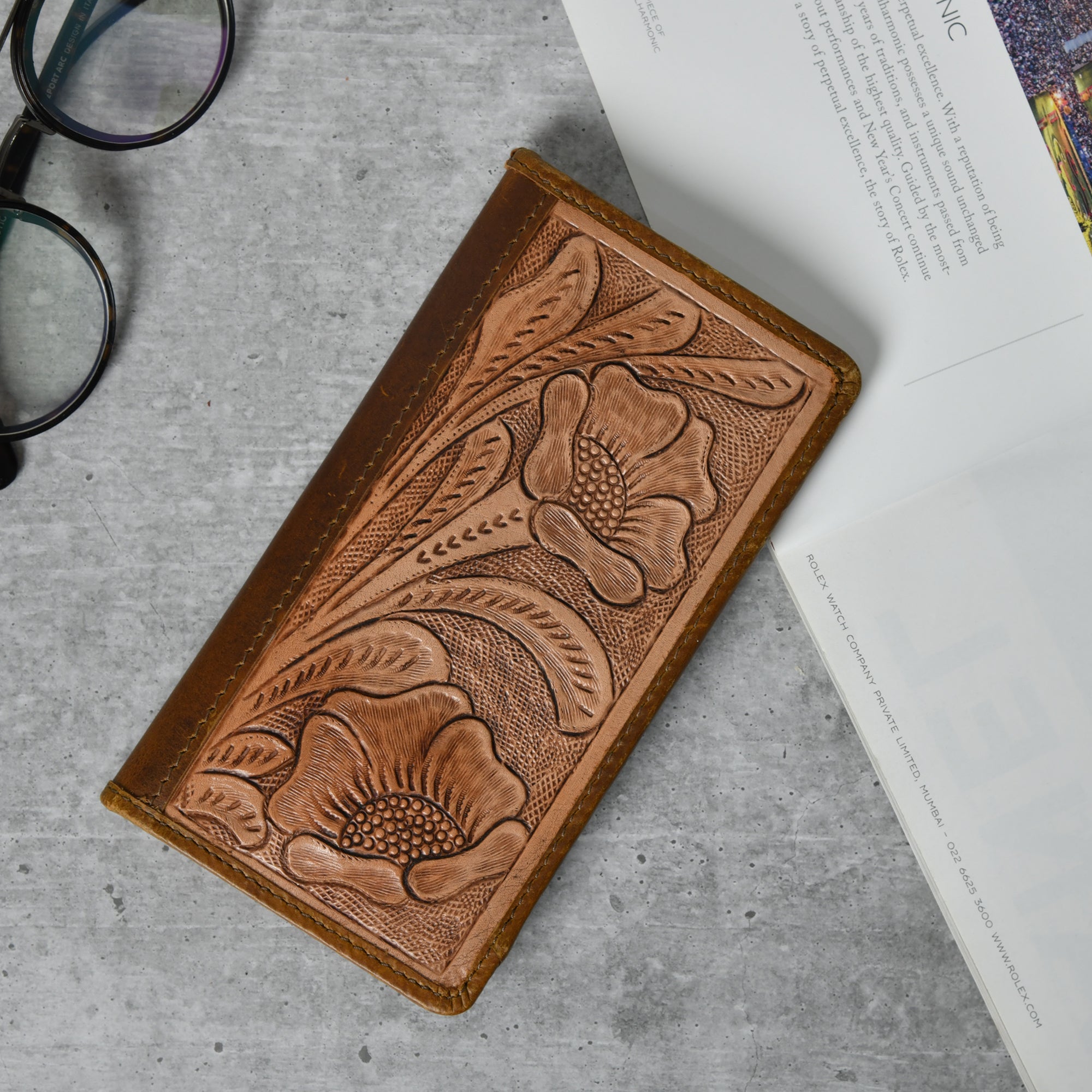 Brown leather bifold wallet with tooled floral design, shown lying open to display card slots and checkbook holder.