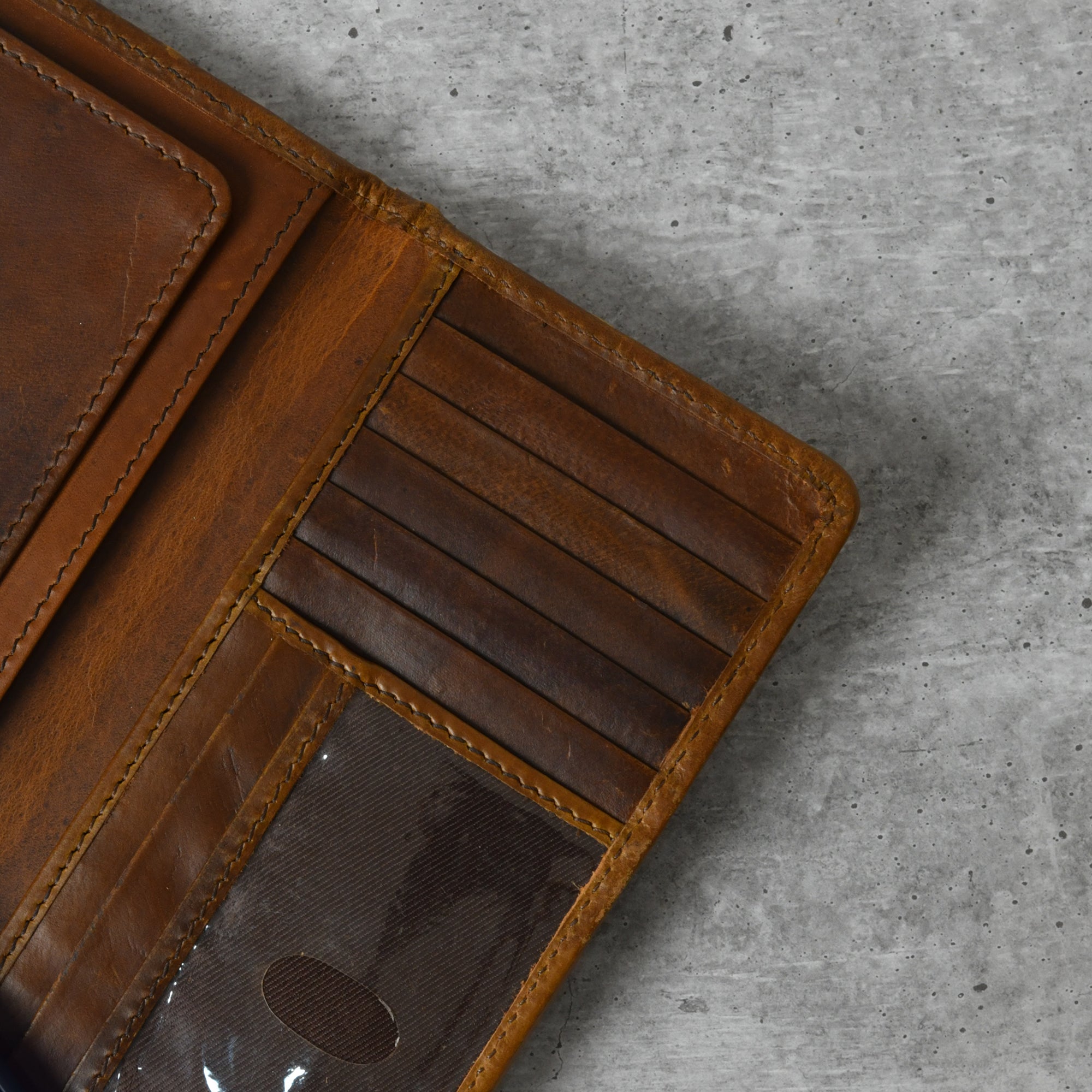 Brown leather bifold wallet open to show multiple card slots and a clear ID window.