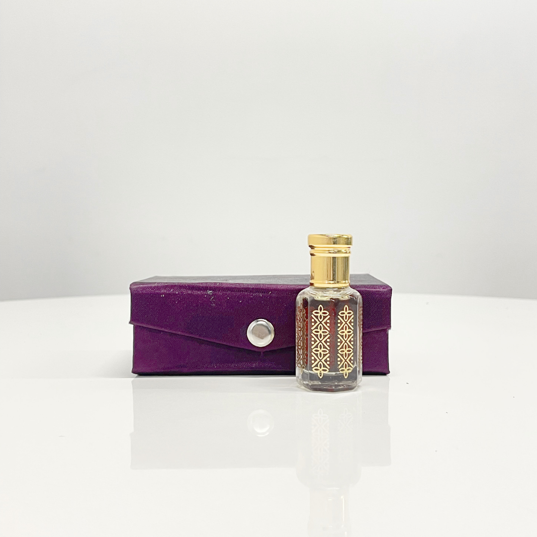 A bottle of Sunshine Attar Unisex perfume, with ornate gold detailing, displayed beside its purple presentation box.