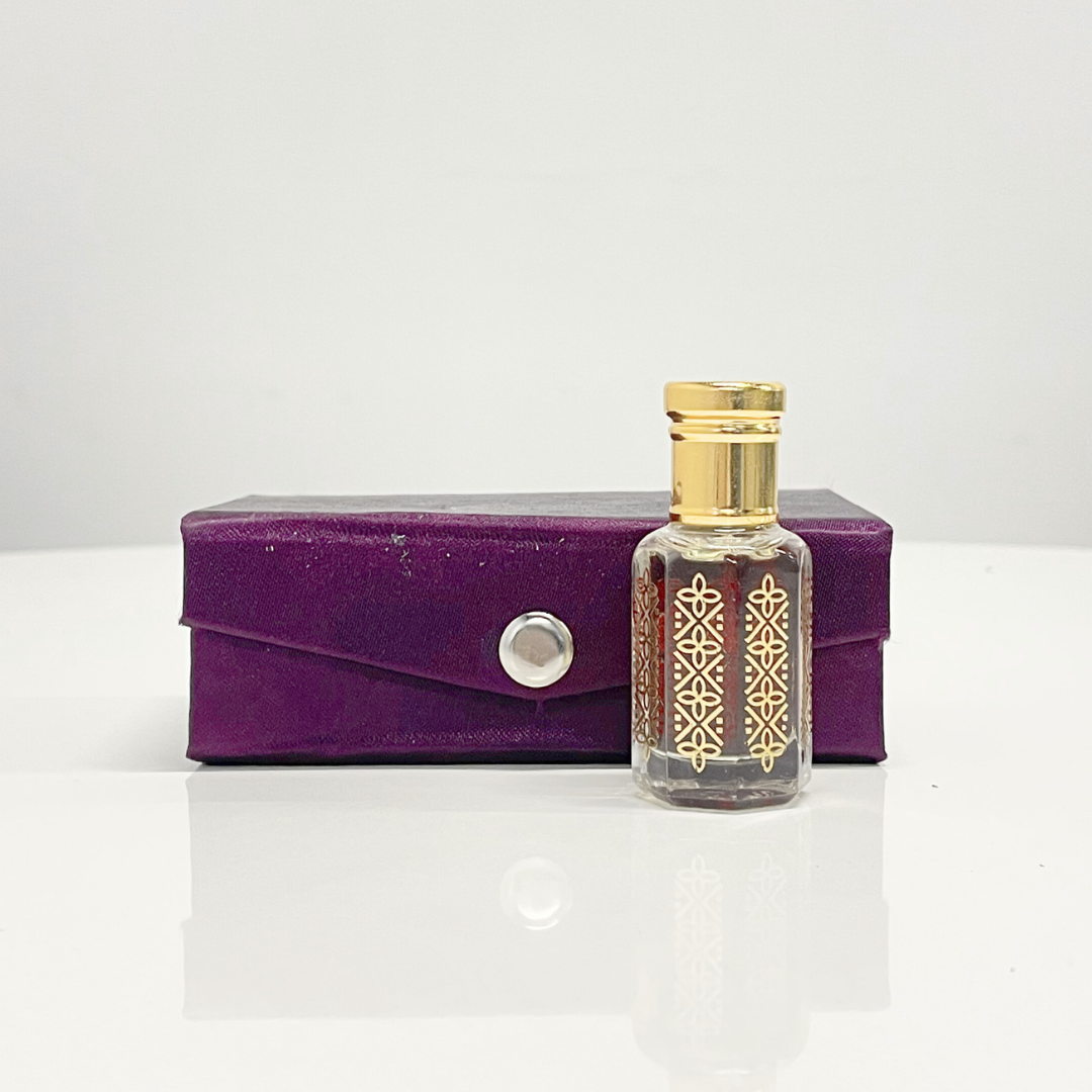 A bottle of Black Oud Attar unisex fragrance with a gold top, beside a purple presentation box.