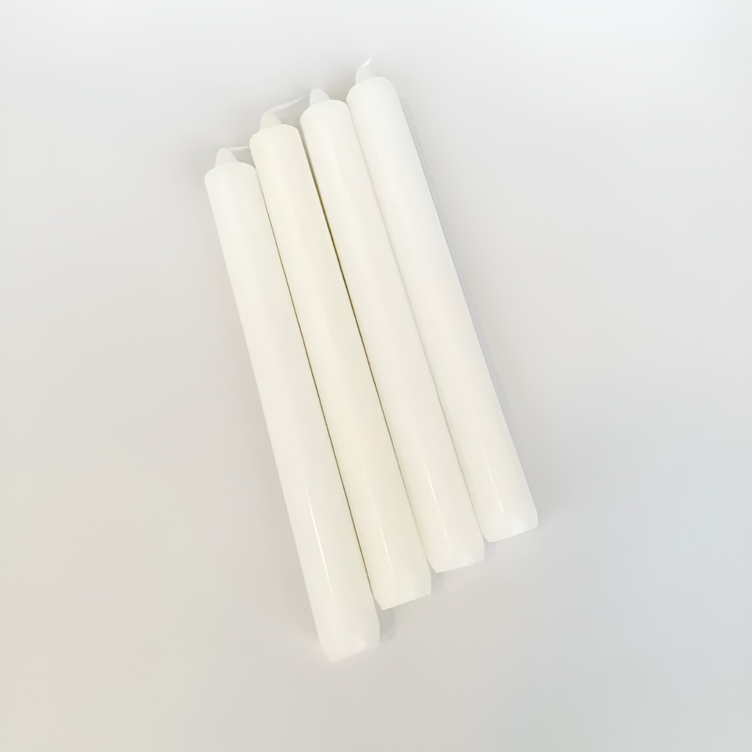 Set of four unscented white paraffin wax candles lie on a white surface.