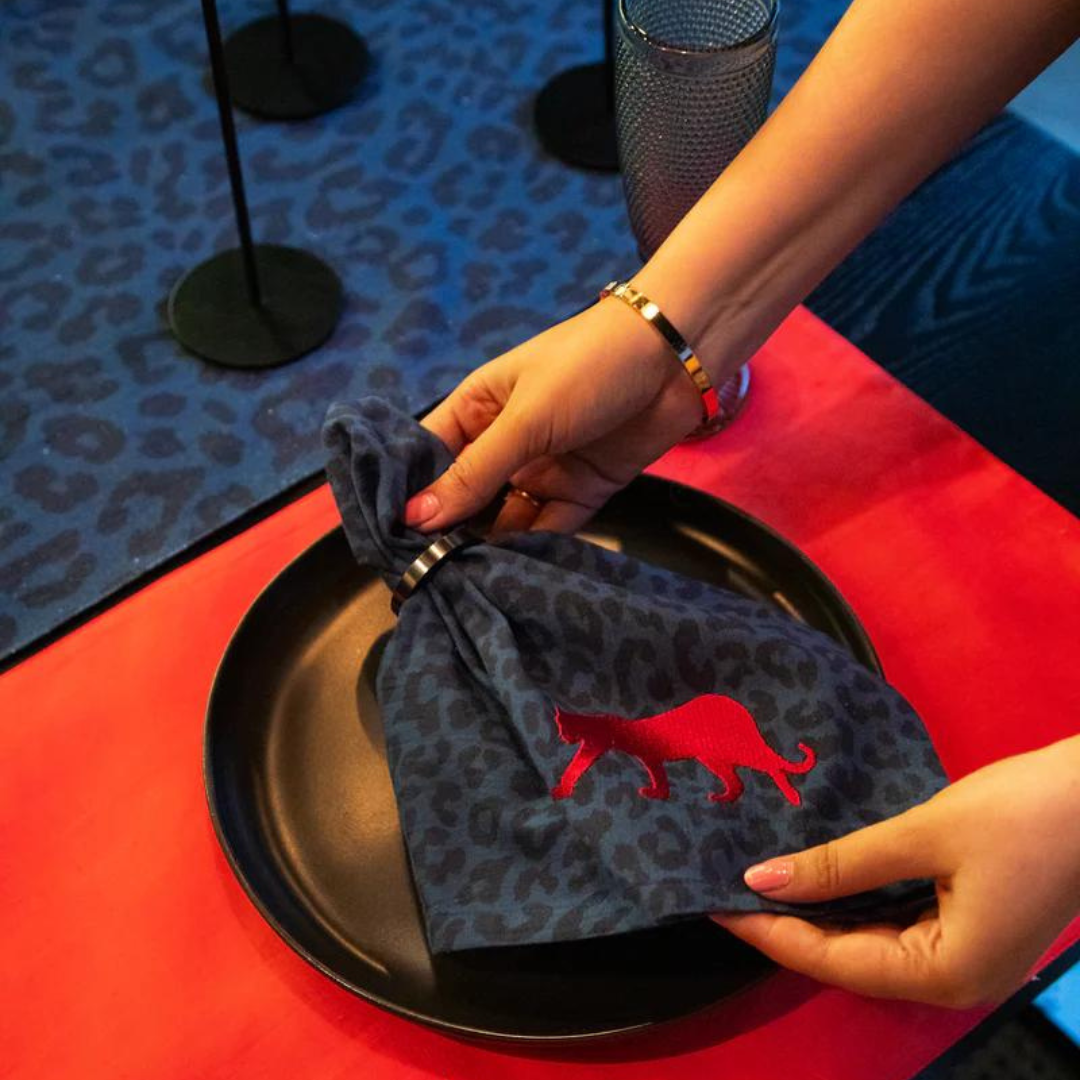 Stylish blue leopard print napkin with red embroidered panther from the Royal Walk Table Linen Set. Set includes placemats, napkins, and a table runner.