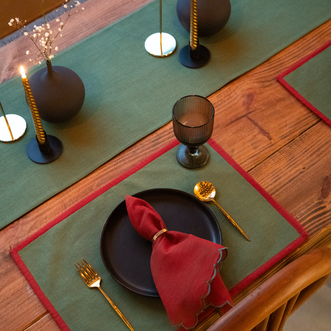 Forest green and red table runner with a subtle border, draped over a wooden table set for a holiday meal.