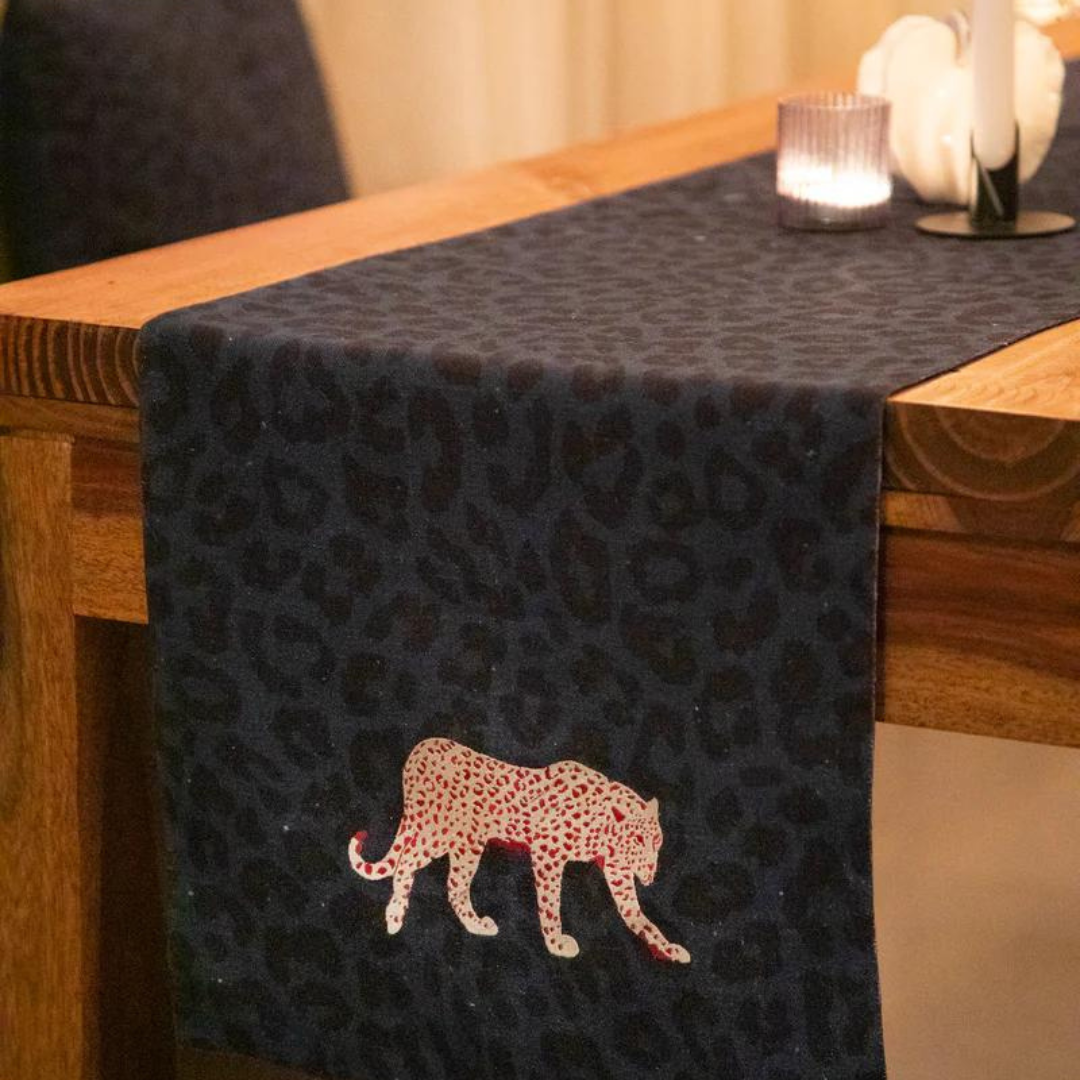 Navy blue cotton table runner with a leopard print and embroidered red and white tiger, draped over a wooden table.