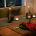 Forest green and red yarn-dyed cotton table runner with red trim, set for a festive meal on a wooden table.