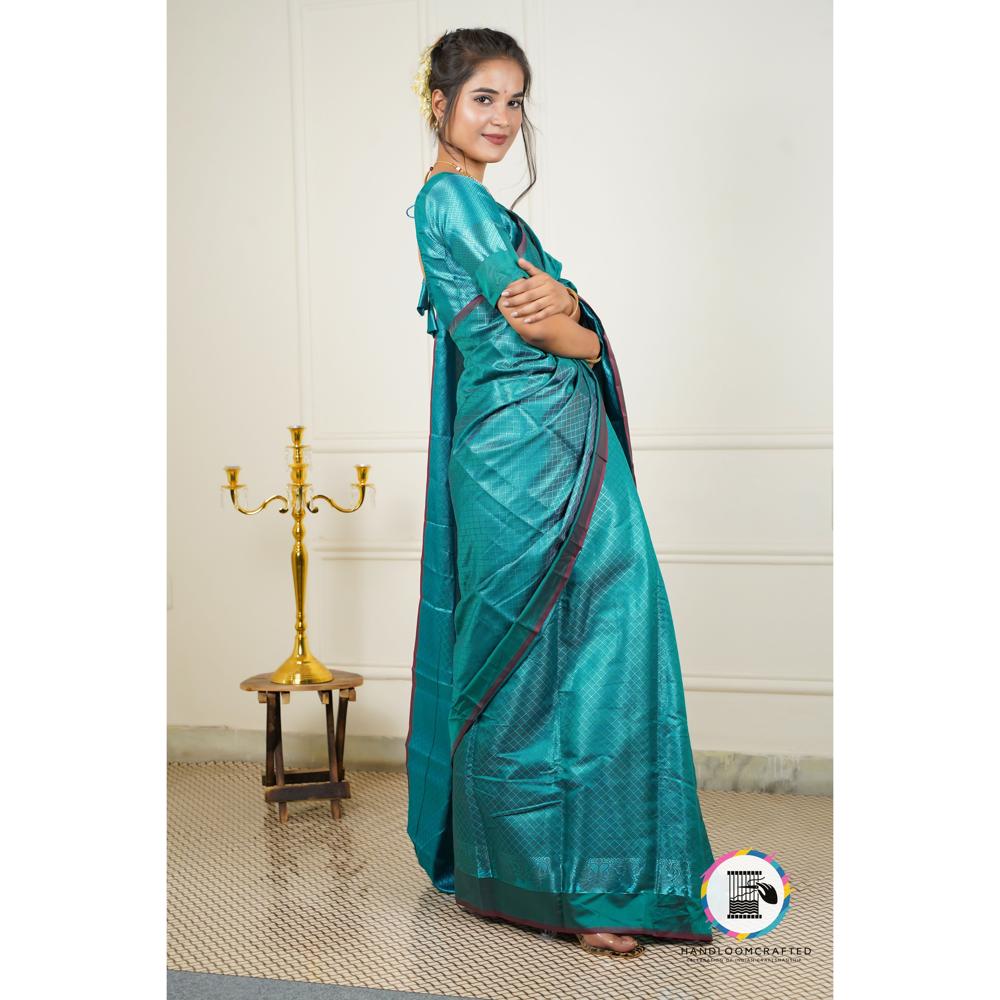 A woman stands elegantly in a dark blue Banarasi tissue silk saree with subtle printed patterns, showcasing the drape and sheen of the fabric.