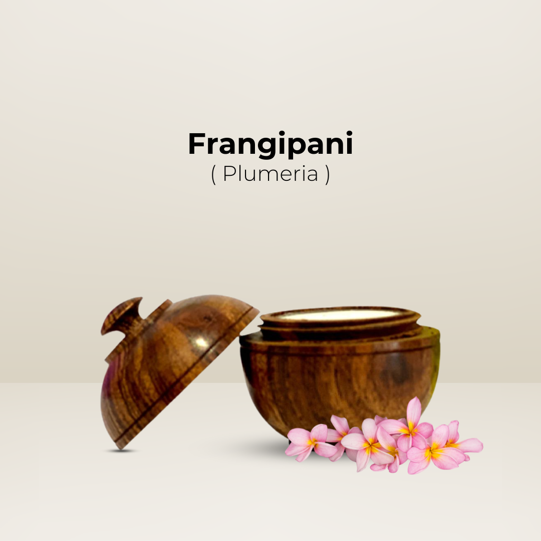 Natural Solid Body Wax Perfume (Frangipani) in an open wooden jar with fresh plumeria flowers beside it.