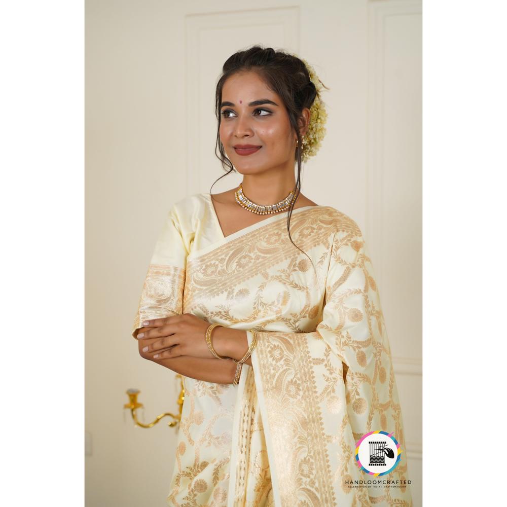 A woman wears an elegant cream Parmigiano Cheese colored Banarasi tissue silk saree with intricate gold floral patterns.