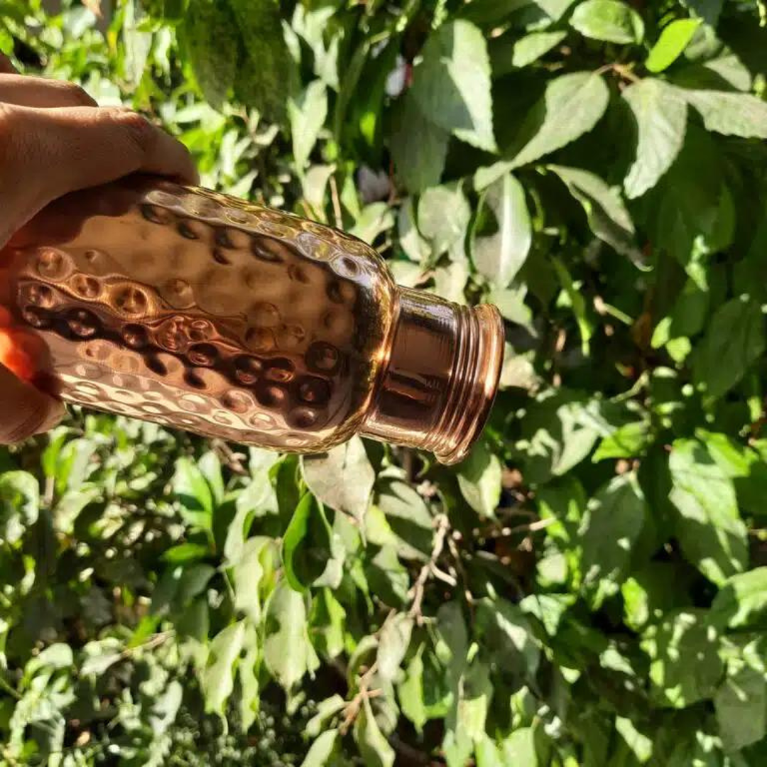 Hand holding a hammered copper water bottle outdoors, showcasing its unique texture.