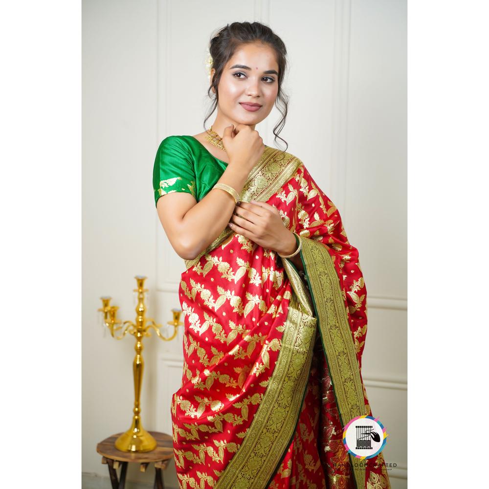 A model poses in a red and green printed Banarasi tissue silk saree, showcasing the intricate gold leaf pattern and rich color combination.