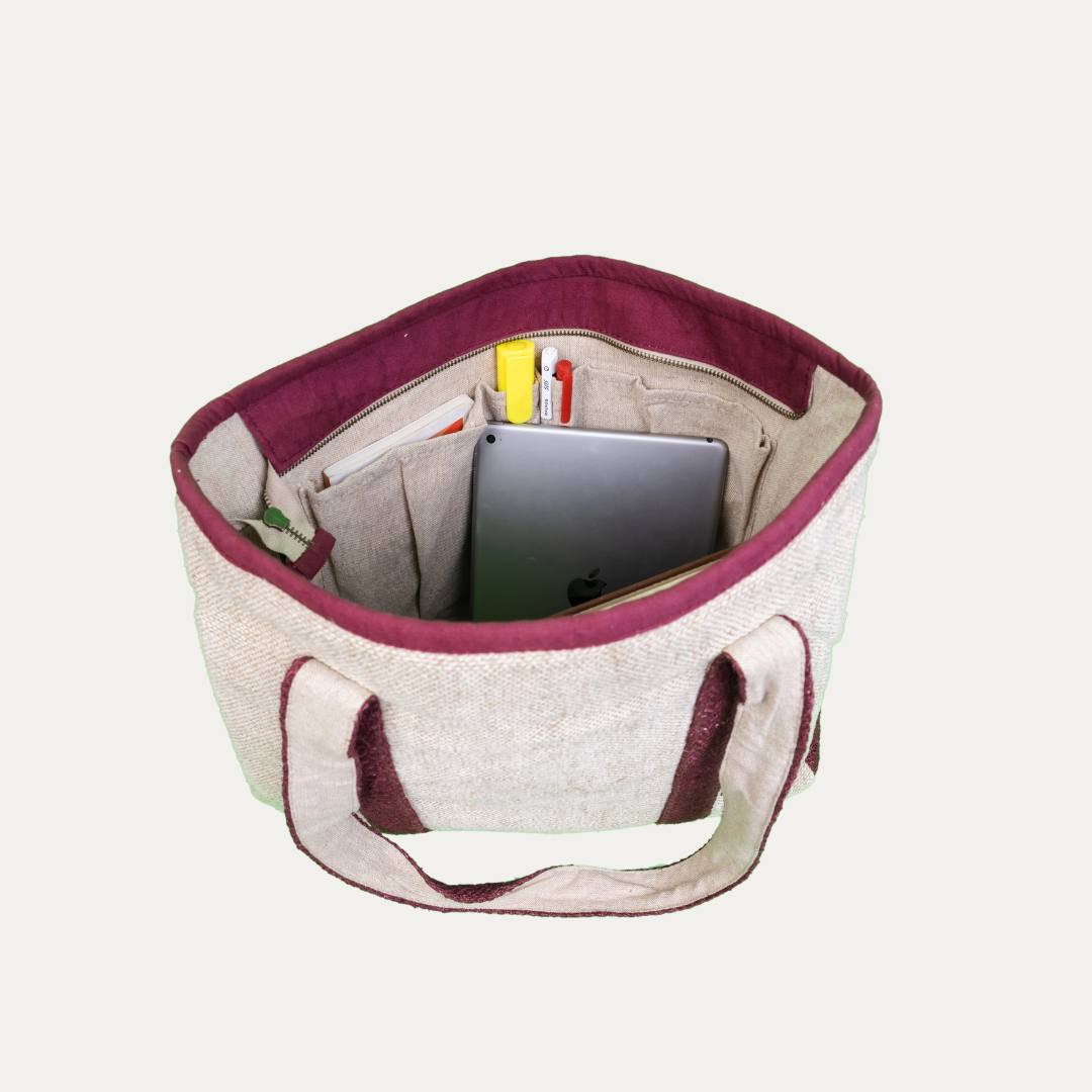 Eco-friendly hemp tote bag with burgundy trim, open and filled with office supplies like a tablet, notepad, and pens.