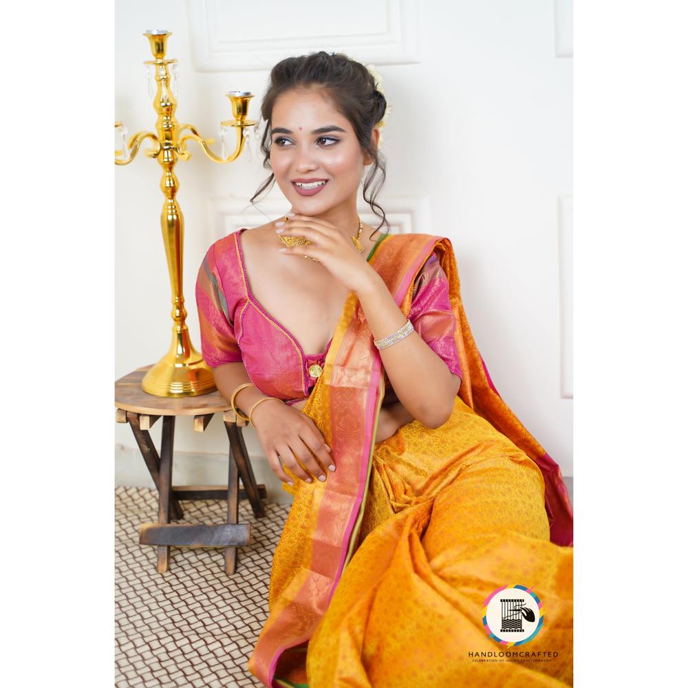 A woman draped in a vibrant yellow Banarasi Tissue Silk Saree with red accents, showcasing its intricate print and luxurious feel.