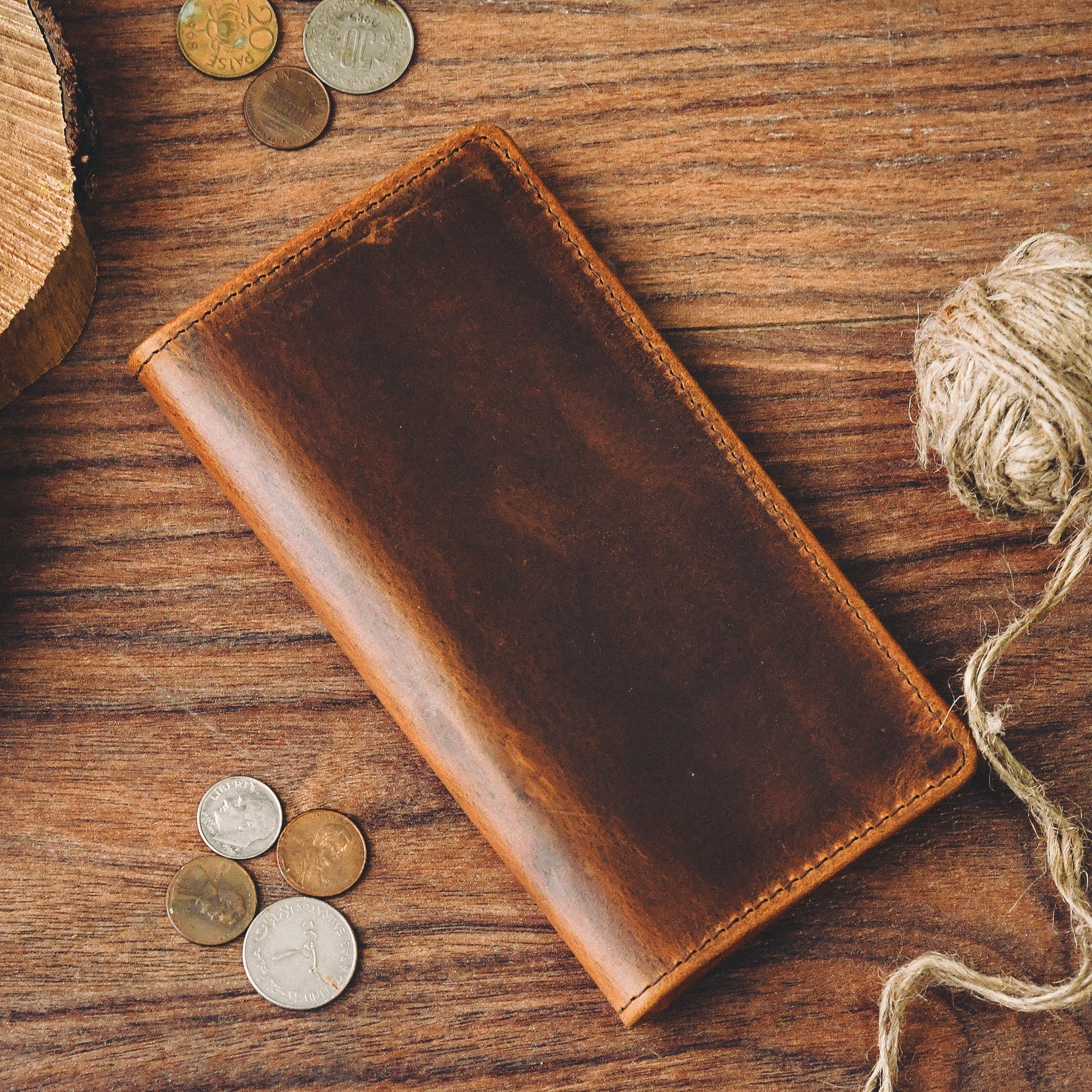 Brown leather bifold wallet lying on a wooden table. The wallet is open to show the multiple card slots and compartments.