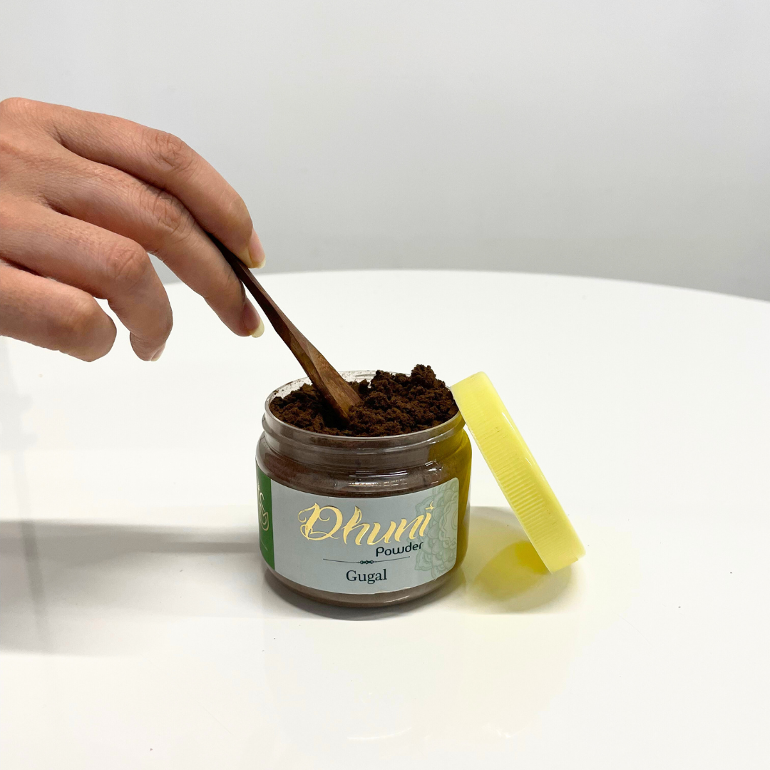 A jar of Gugal Dhuni Powder (Bakhoor) with a wooden spoon scooping out the aromatic incense powder.