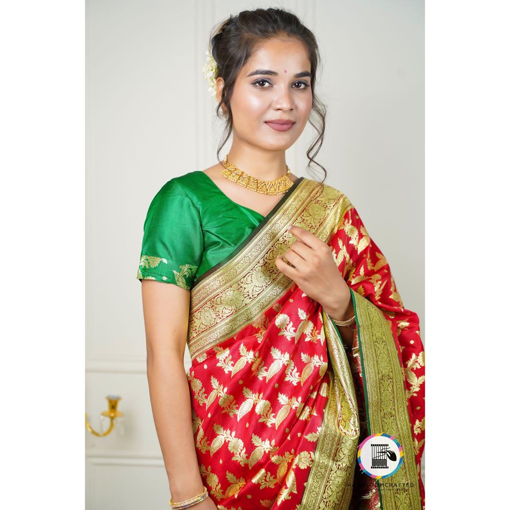 A woman in a green blouse drapes a red and green "Green Red Printed Soft Banarasi Tissue Silk Saree," showcasing its intricate floral print and golden border.