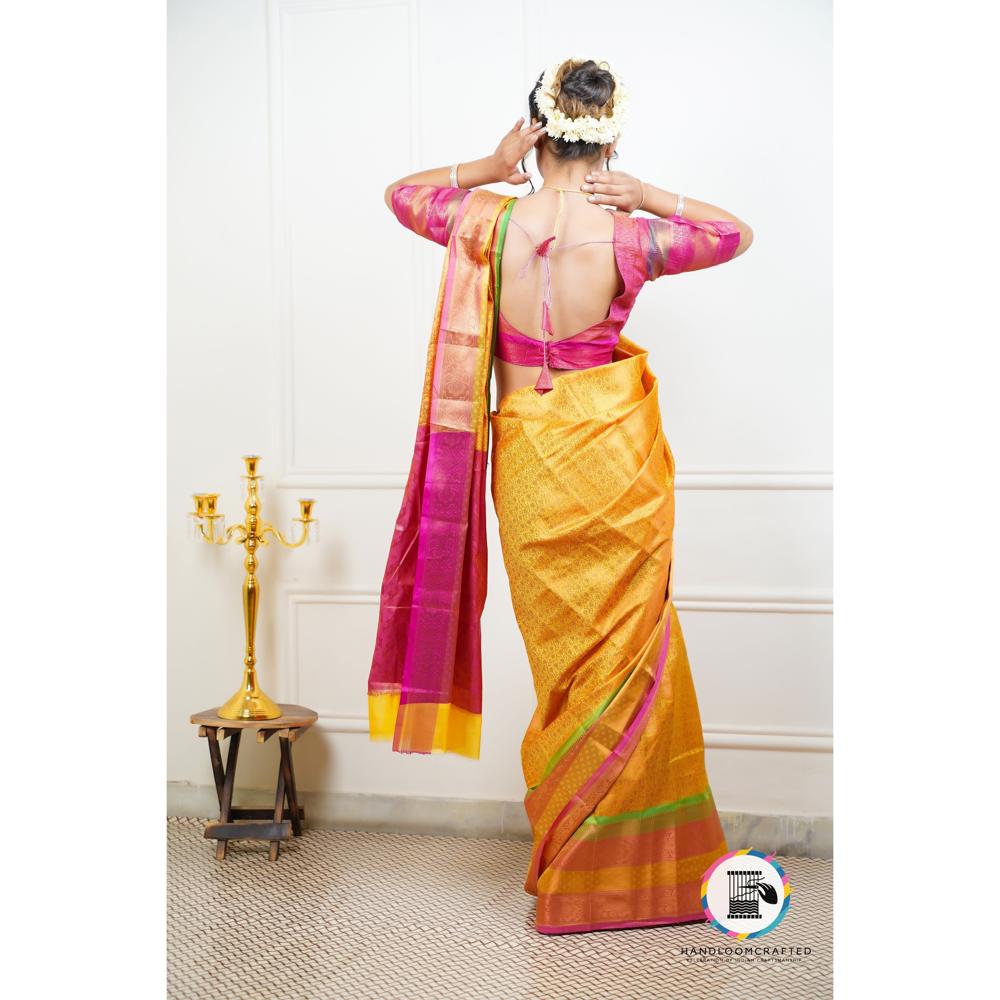 A woman models a vibrant yellow Banarasi tissue silk saree with red and pink accents, showcasing the drape and intricate design.