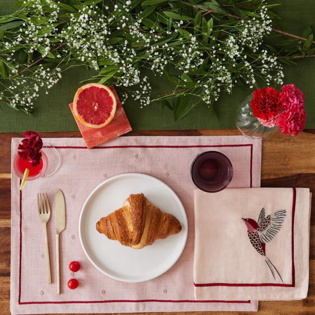 Scarlet French linen table runner, placemats, and napkins with embroidered bird detail set a romantic table for a meal.