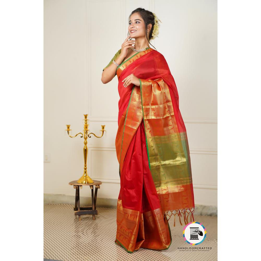 A woman stands elegantly draped in a red Banarasi tissue silk saree, accented with green and gold printed designs.