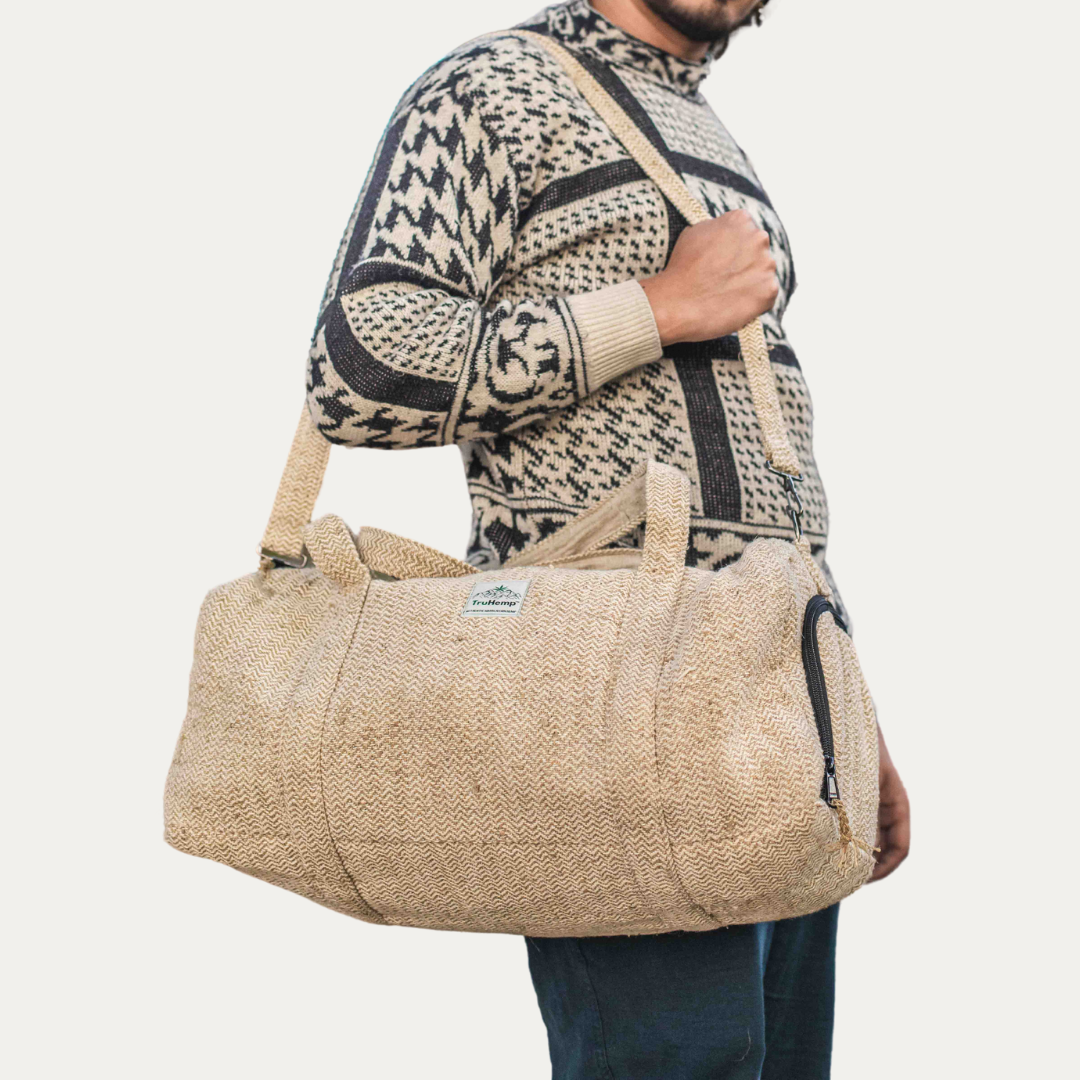 A man models a spacious, eco-friendly hemp duffle bag in a natural beige color. The bag features a dedicated shoe pocket and sturdy shoulder strap.