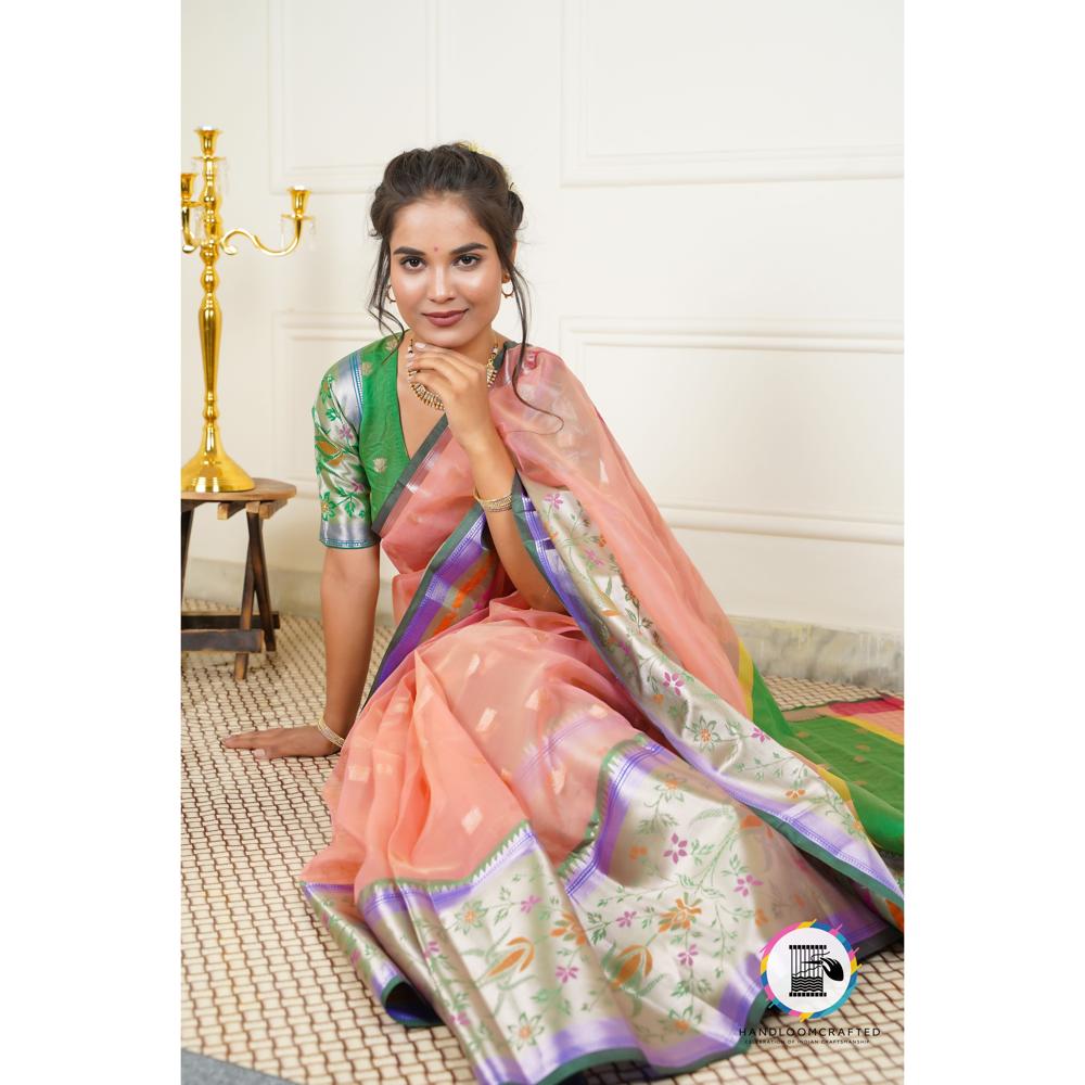 A woman poses gracefully in a peach-colored "Green Peach Printed Soft Banarasi Tissue Silk Saree," showcasing its intricate floral print and vibrant green border.