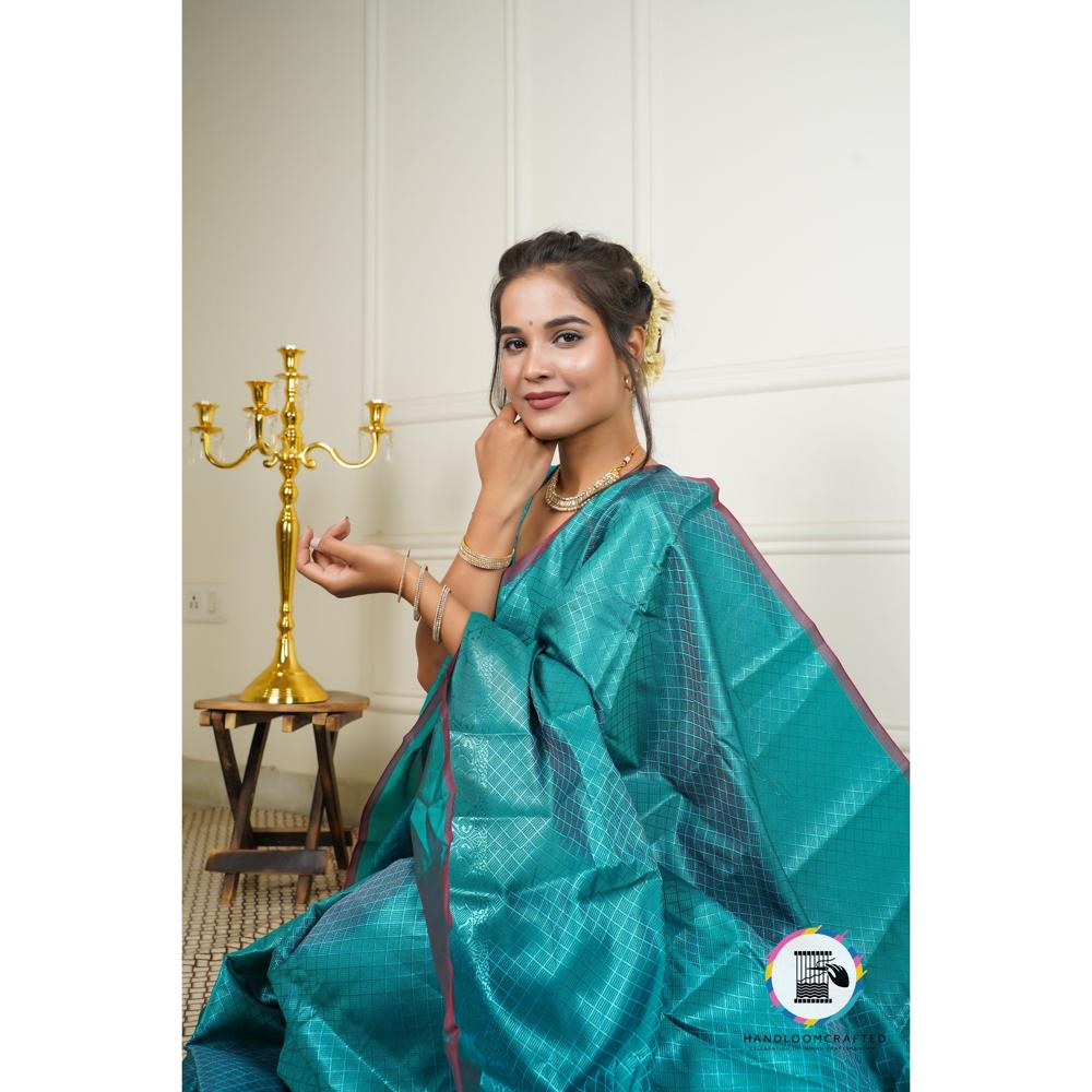 A woman poses gracefully in a dark teal blue Banarasi tissue silk saree with a subtle woven pattern, highlighting its elegance and drape.