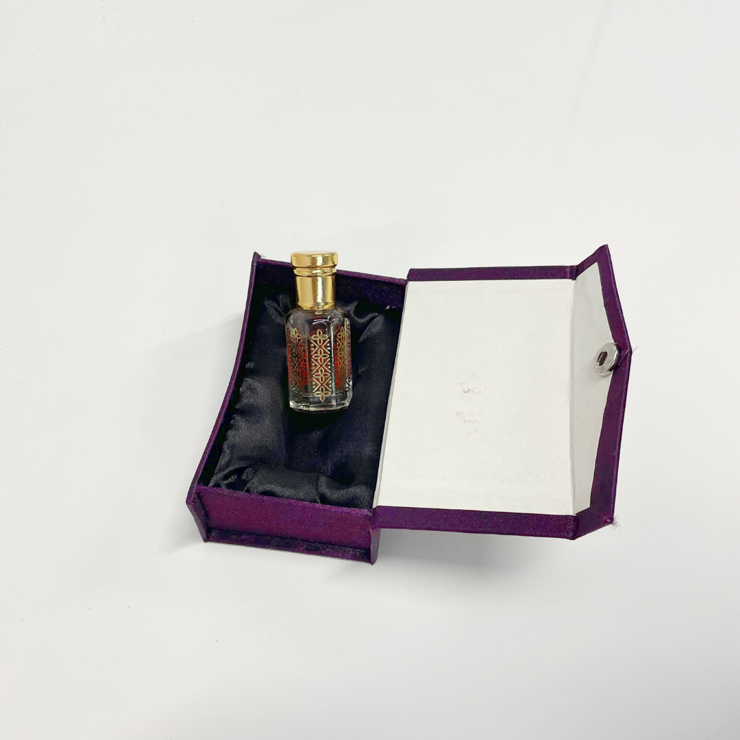 Sandalwood Attar Unisex perfume in an ornate glass bottle, nestled in a luxurious purple presentation box.