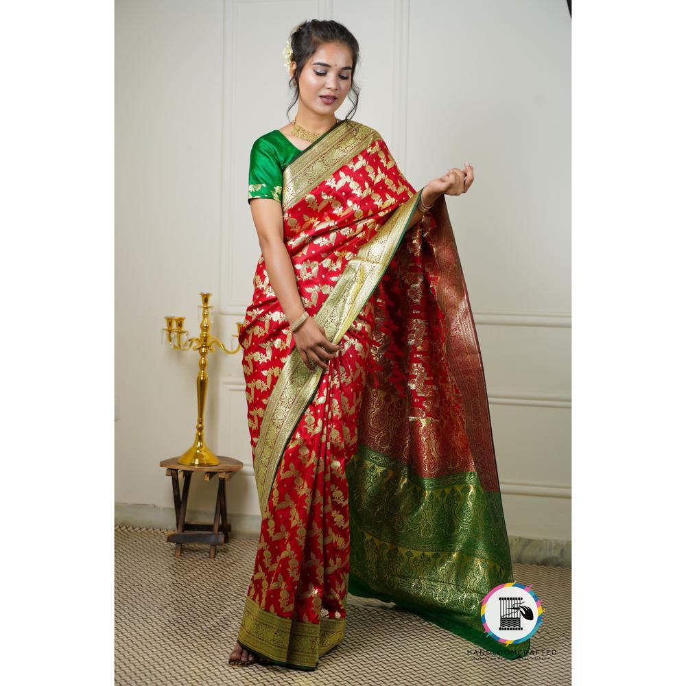 A woman stands modeling a red and green printed Banarasi tissue silk saree with gold accents.