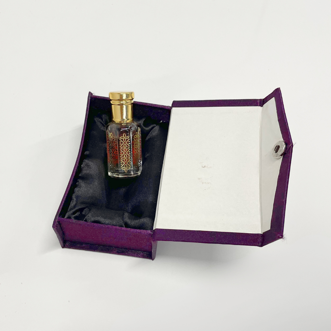 Black Oud Attar in an ornate glass bottle, nestled in a luxurious purple presentation box.