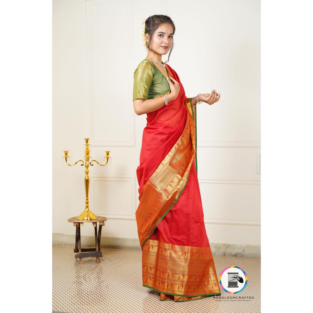 A woman stands elegantly in a red and green Banarasi tissue silk saree, featuring intricate gold printed patterns, reflecting its premium quality and traditional design.