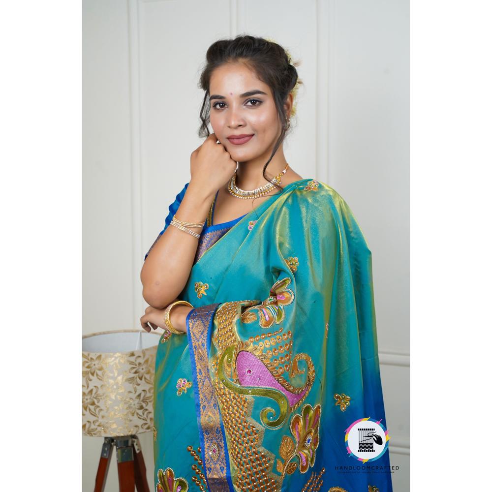 Woman wearing a peacock blue Banarasi tissue silk saree with intricate embroidery and embellishments.