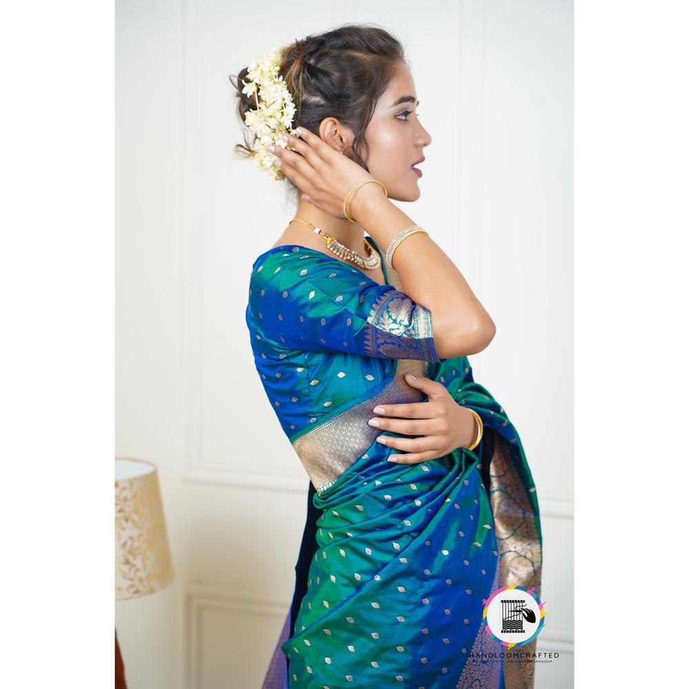 A woman poses in a blue and green Banarasi tissue silk saree with a printed pattern, showcasing its elegant drape and intricate design.