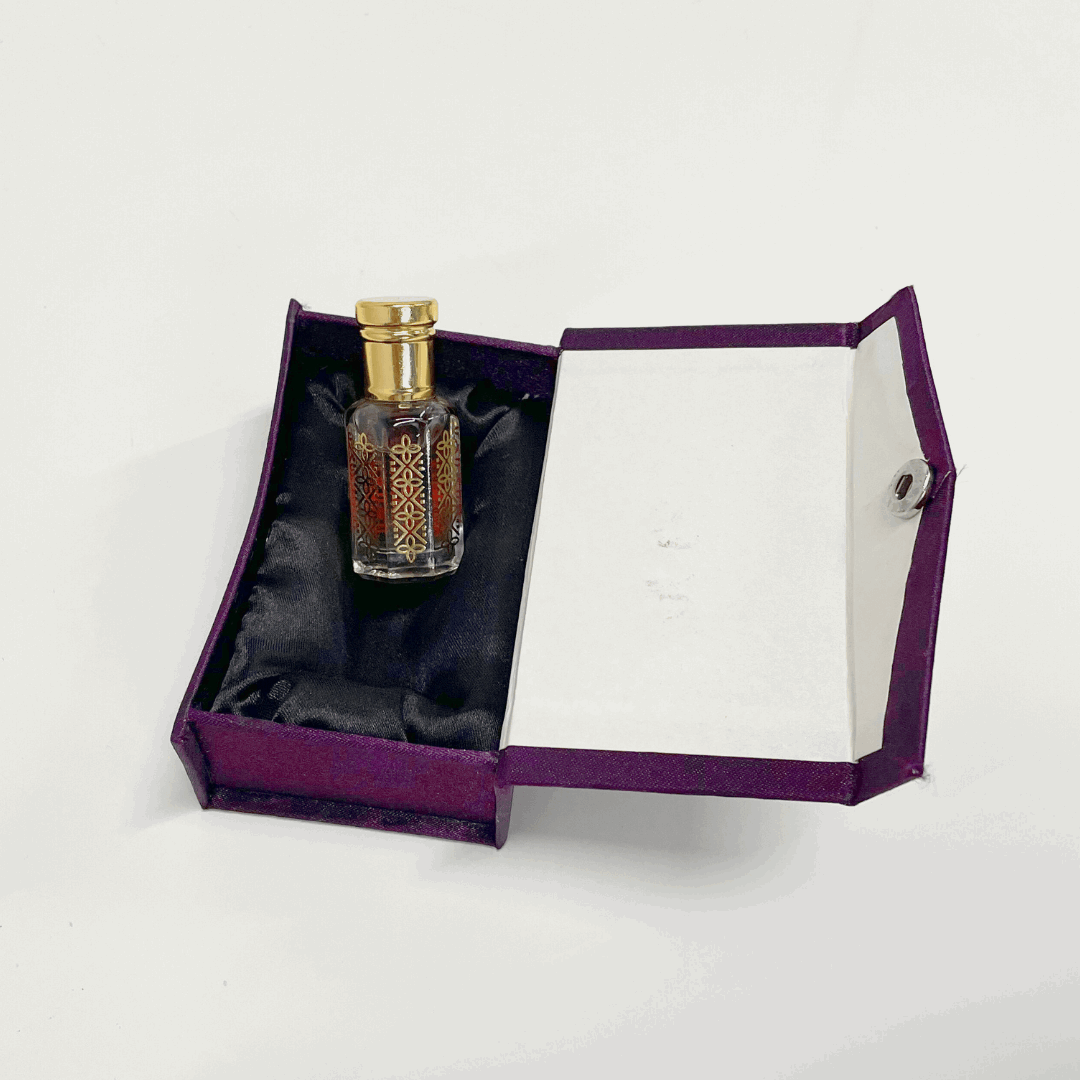 Black Oud Attar in an ornate glass bottle, nestled in a luxurious purple presentation box.