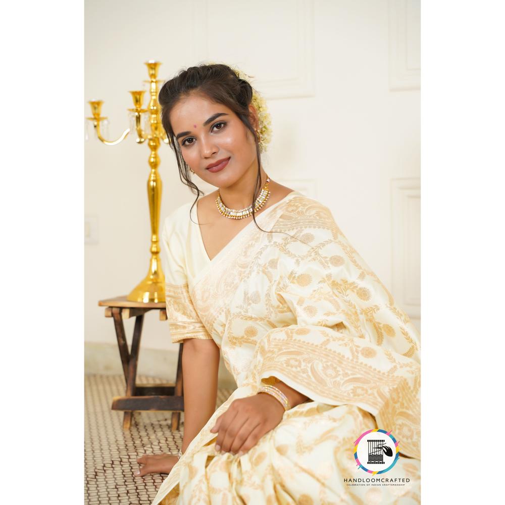 A woman poses gracefully in a cream Parmigiano Cheese colored Banarasi Tissue Silk Saree, showcasing its intricate gold floral patterns.