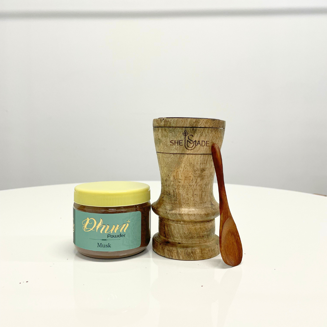 A jar of Musk Dhuni Powder sits beside a wooden dhuni burner and small spoon, ready to fill your home with a warm, musky aroma.