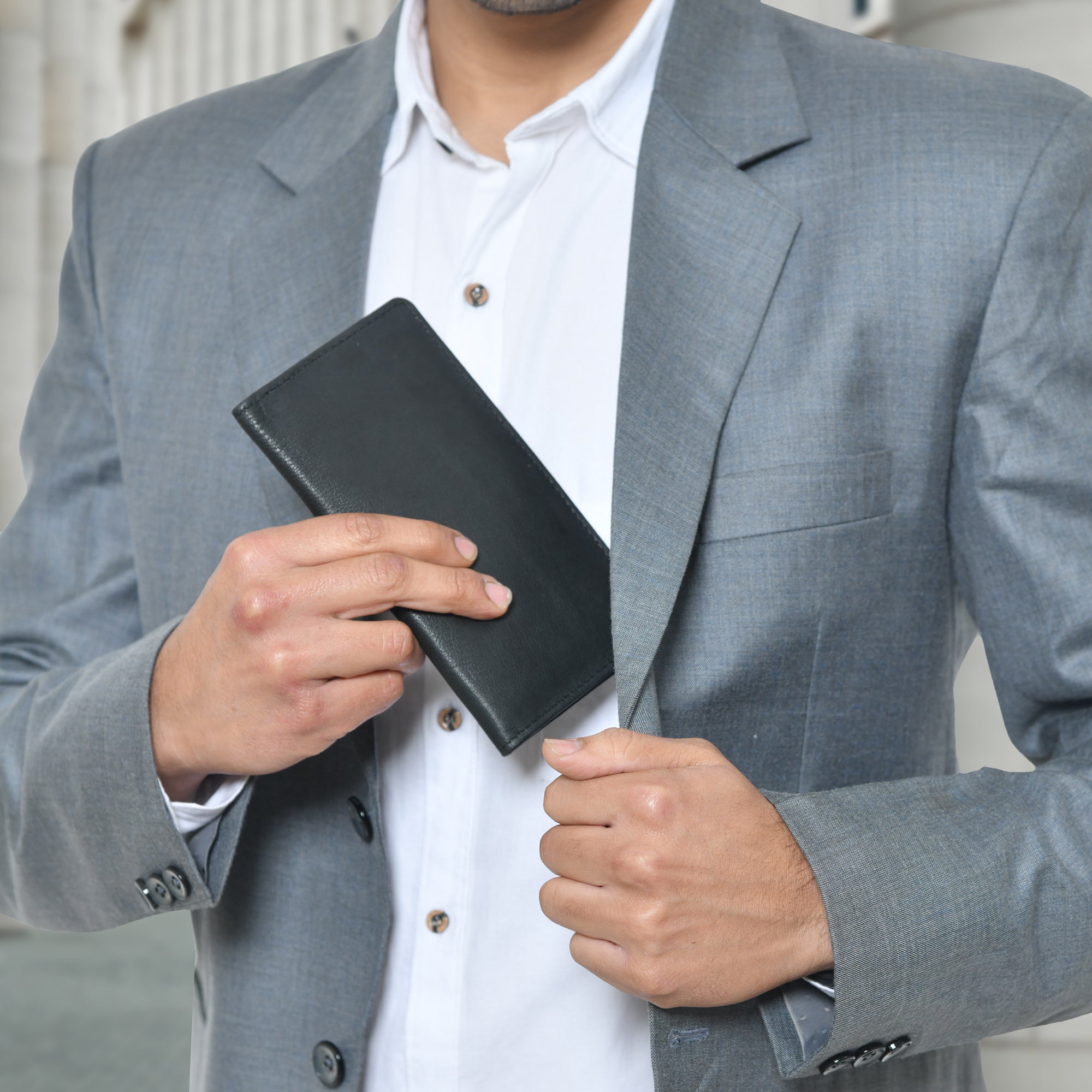 A man putting a black leather bifold wallet into his suit jacket pocket. The wallet has 11 compartments for cash, cards, and a checkbook.