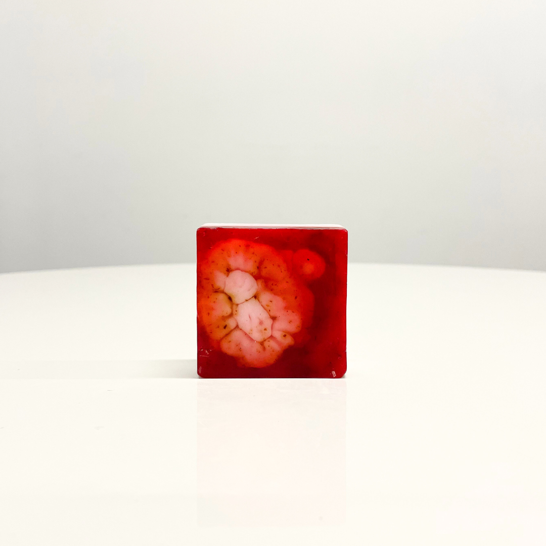 A single bar of red and pink Rose & Shea Butter Handcrafted Soap sits on a white table.