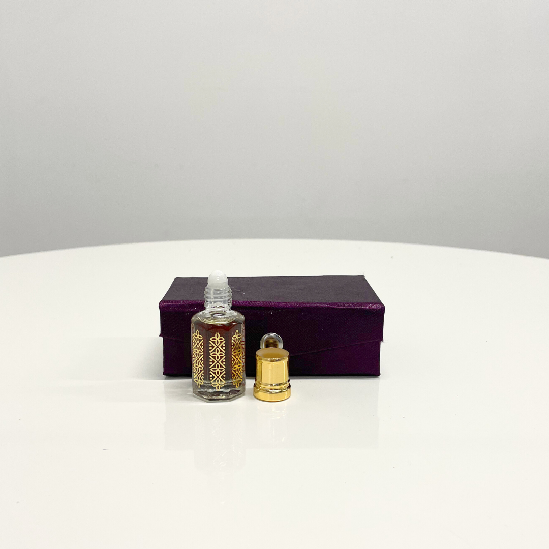 A bottle of Khus Attar Unisex perfume with gold detailing, beside its gold cap and presented on a purple box.