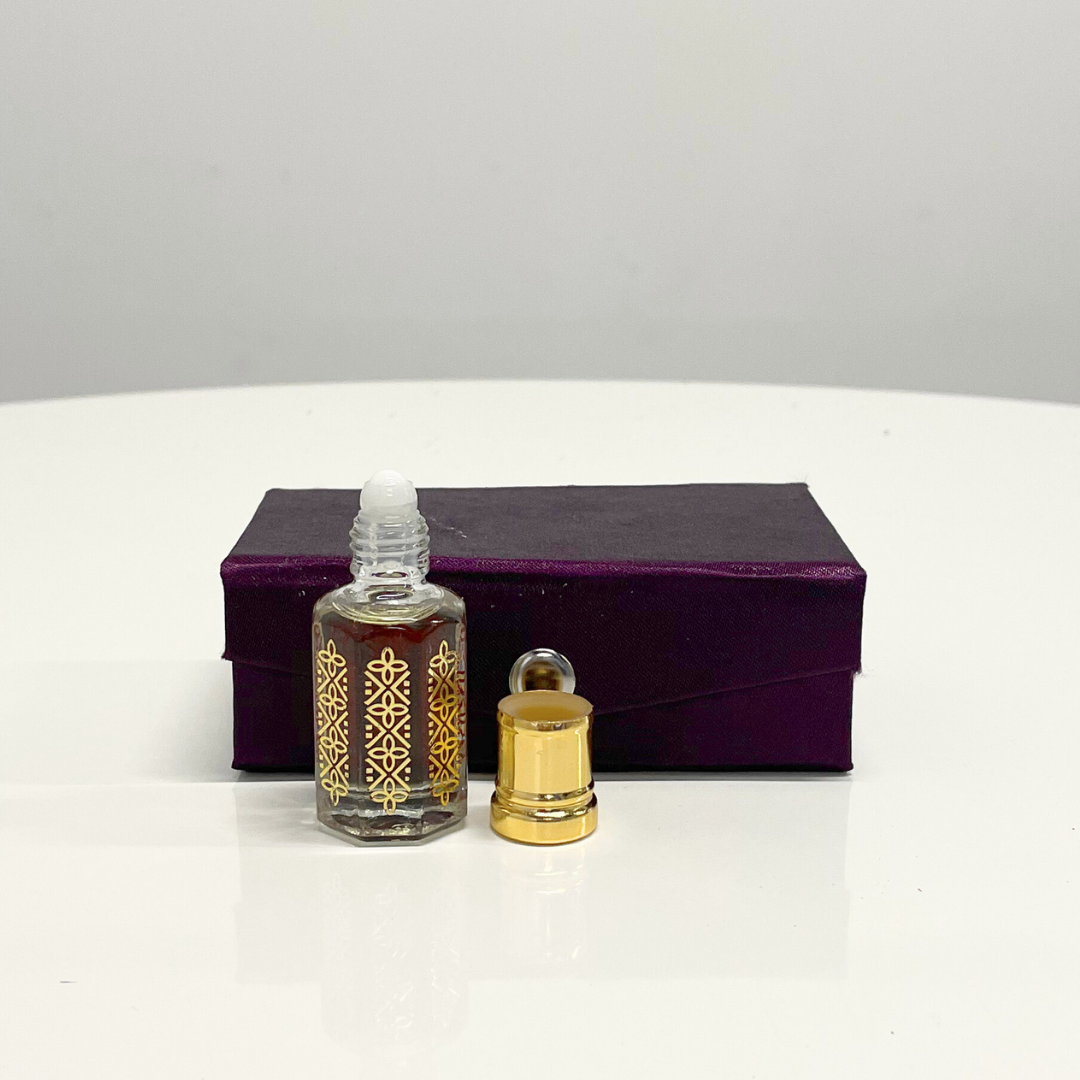 A bottle of Black Oud Attar unisex fragrance with its gold cap off, presented in a luxurious purple box.