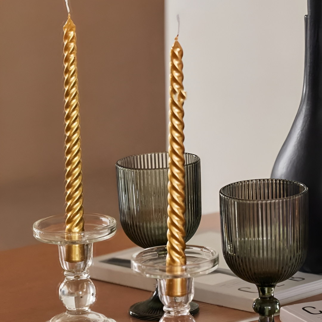 Set of four gold twisted taper candles stand unlit in glass candle holders. These dripless and smokeless candles add elegant ambience.