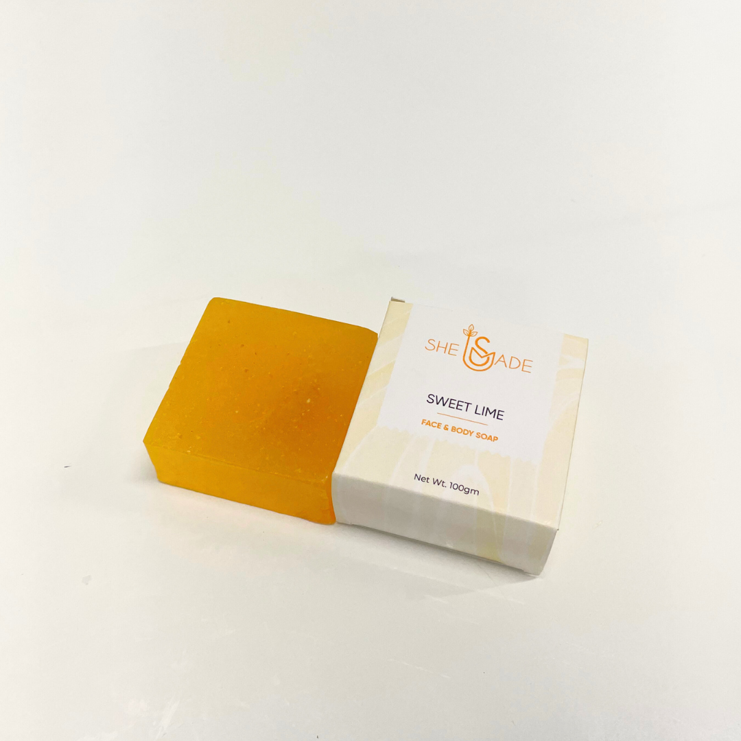 A handcrafted bar of Sweet Lime Soap sits outside its box. The soap is bright orange and speckled.