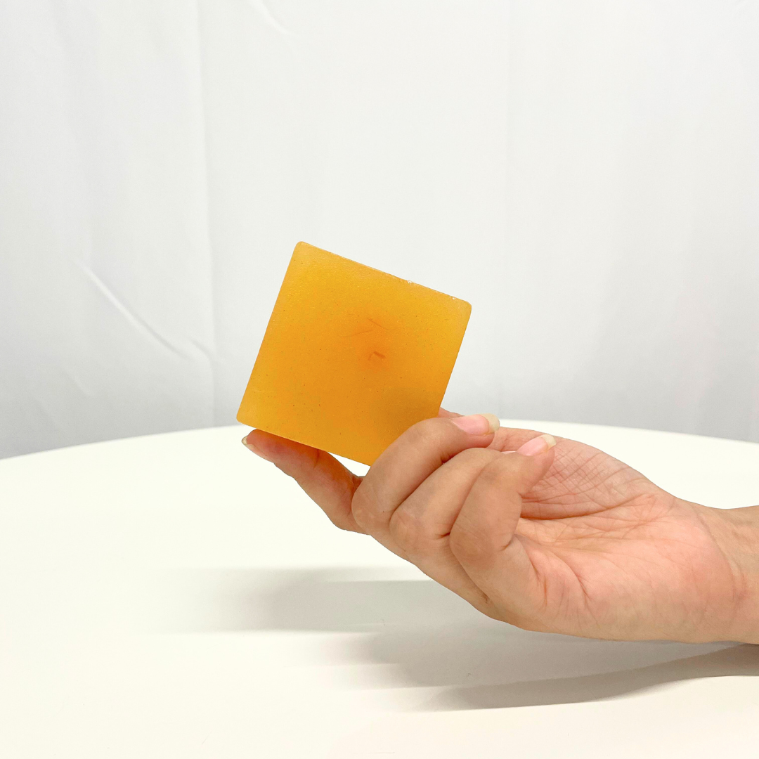 Hand holding a square bar of golden-orange Saffron Turmeric Handcrafted Soap.