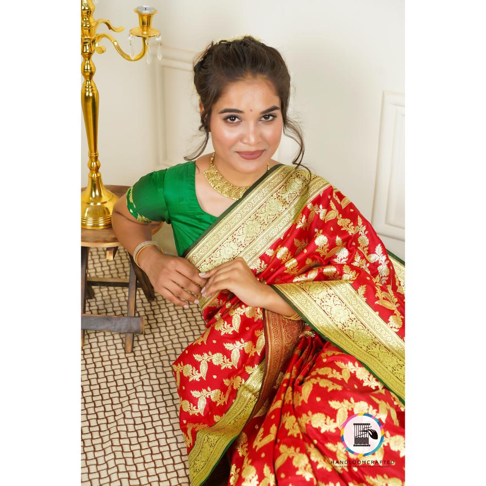 A woman poses gracefully in a red and green Banarasi tissue silk saree, featuring intricate gold floral prints and a rich border, showcasing its luxurious texture and drape.