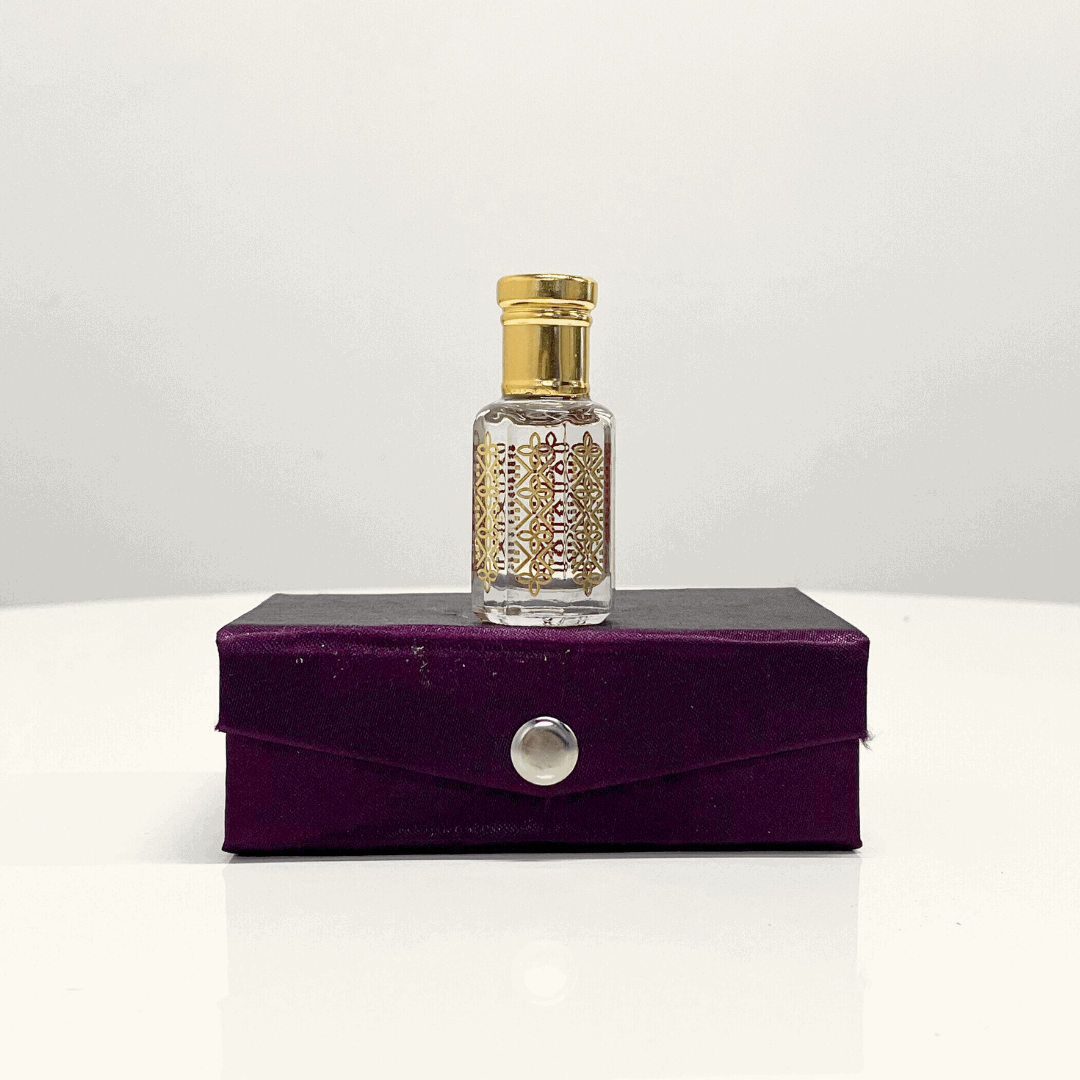 A bottle of Black Oud Attar unisex fragrance with a decorative gold top, resting on a purple velvet presentation box.