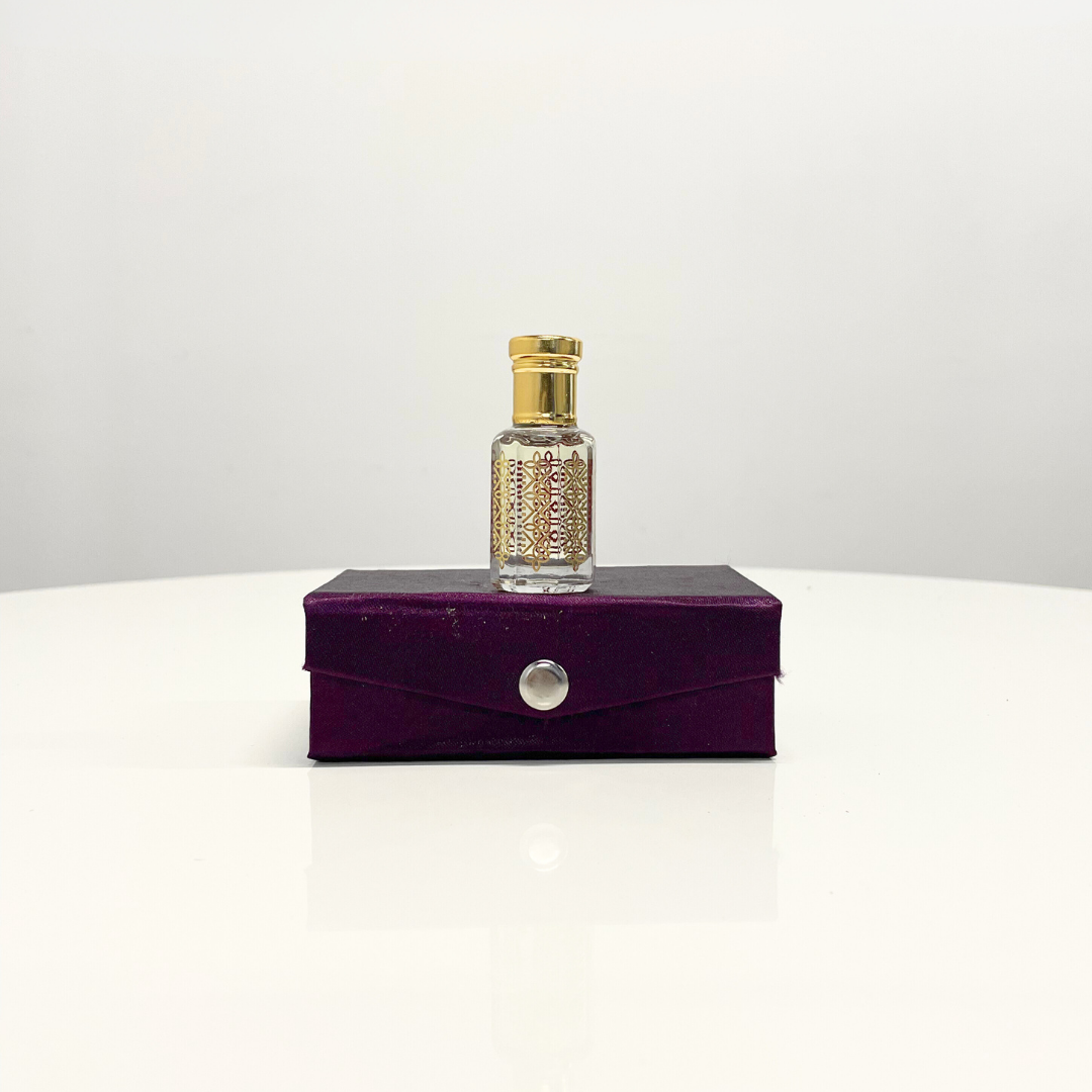 Elegant glass bottle of White Oud Attar unisex perfume with a gold top, displayed on a purple presentation box.