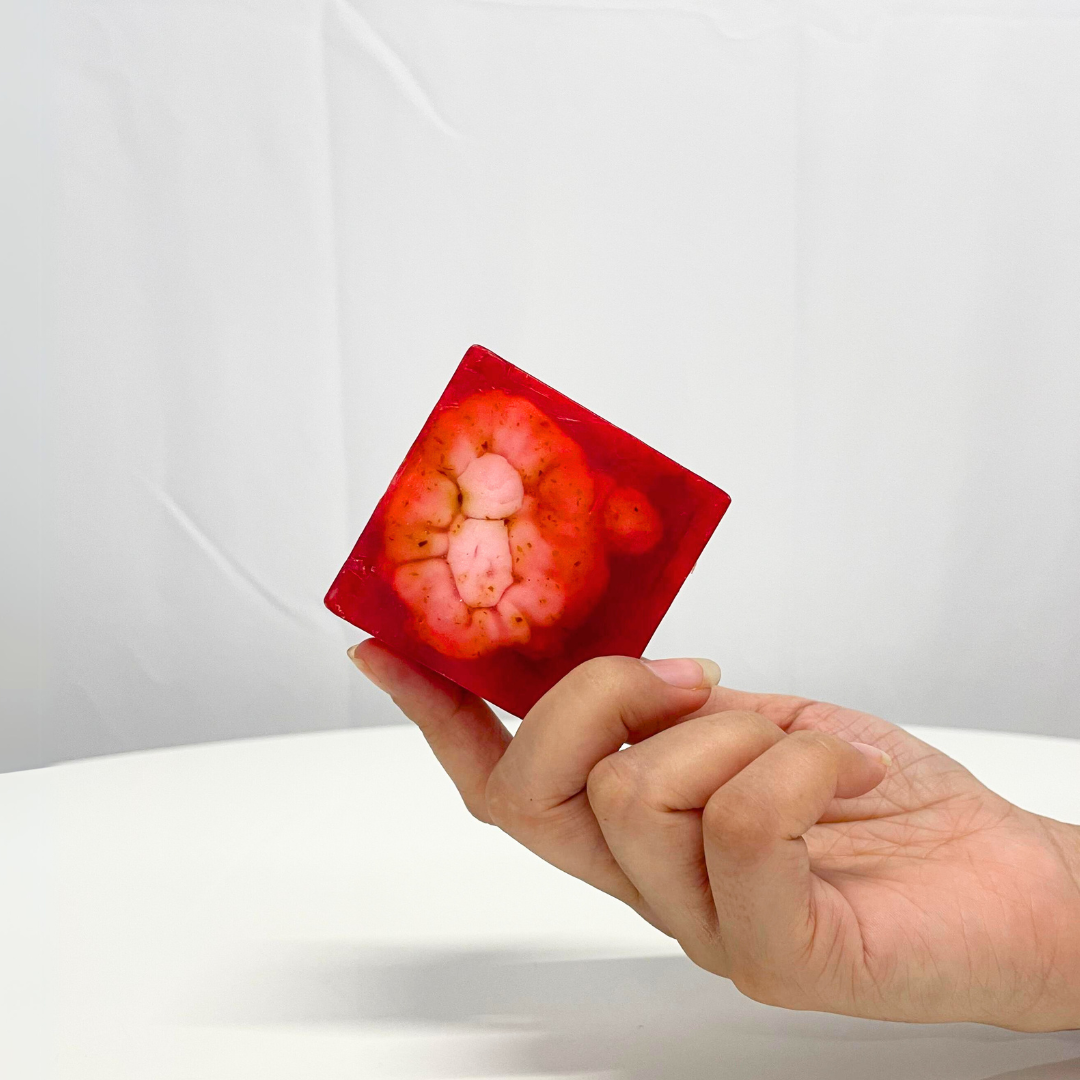 Handcrafted red Rose & Shea Butter Soap held between fingers, showcasing the soap's unique design.