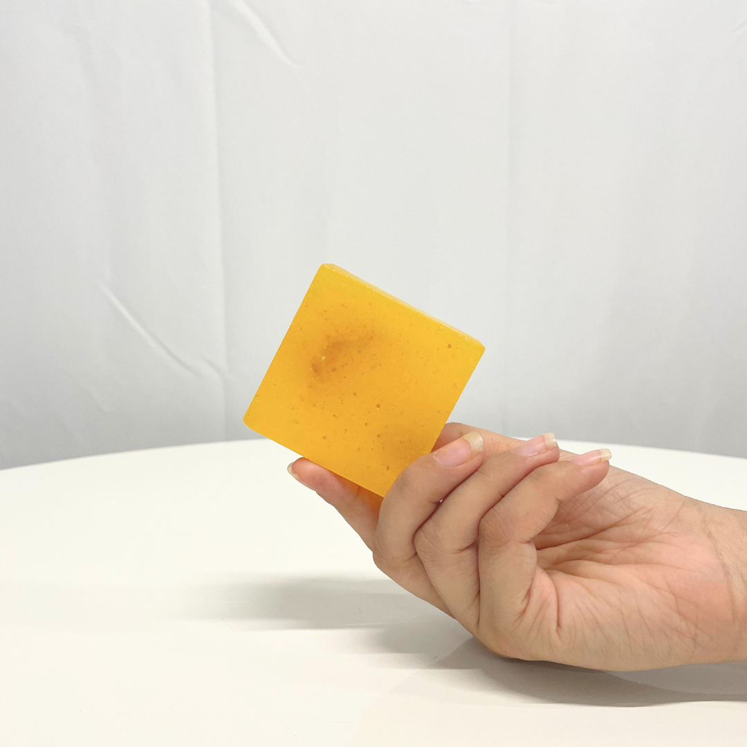 Hand holding a square bar of bright yellow Sweet Lime Handcrafted Soap.