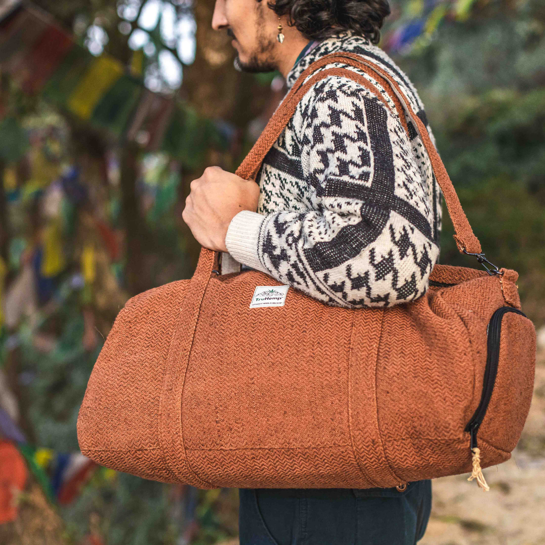 A person carries a durable, rustic-brown Eco-friendly Hemp Duffle Bag with a dedicated shoe pocket, perfect for eco-conscious travel.