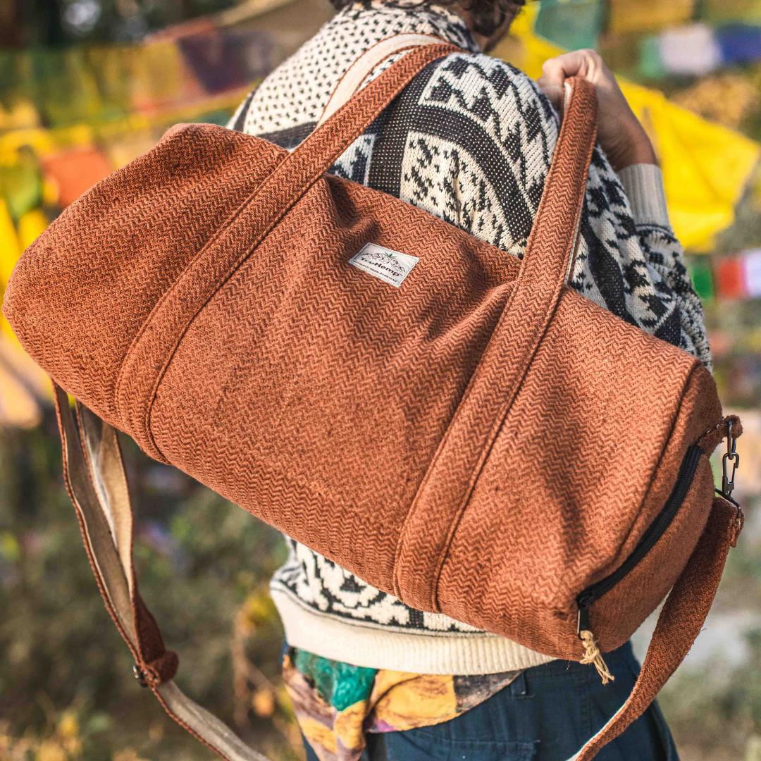 Eco-friendly brown hemp duffle bag with shoulder strap and separate shoe pocket, held by a person.