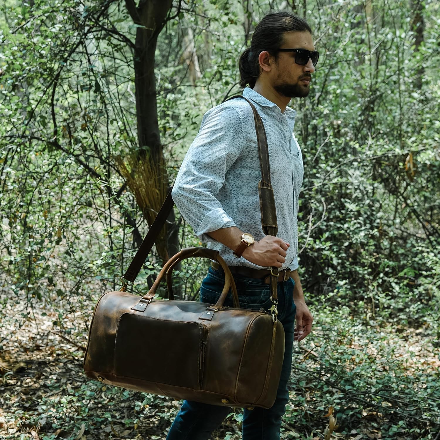 Stylish brown leather weekender duffel bag with multiple pockets, carried by a man walking through nature.